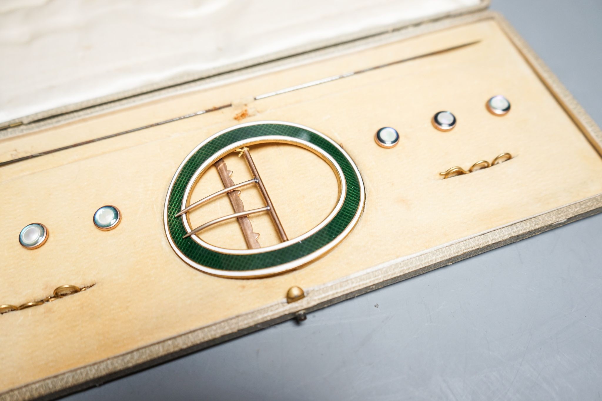 An early 20th century cased gilt metal and enamel buckle, buttons and hat pin set, case 30cm